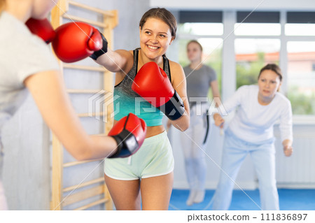 Adolescent girl in boxing gloves practicing punches in sparring during self defence course Adolescent girl in boxing gloves practicing punches in sparring during self defence course 111836897
