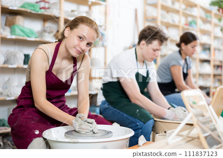 Young woman teacher and two teenagers make products on potter's wheel 111837123