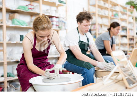 Young woman teacher helps teenagers boy and girl to make product on potter's wheel 111837132
