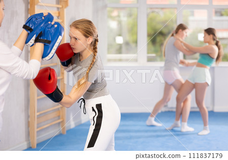 Girls works out strength and speed of boxing punch mitts with help of partner in boxing paws Girls works out strength and speed of boxing punch mitts with help of partner in boxing paws 111837179