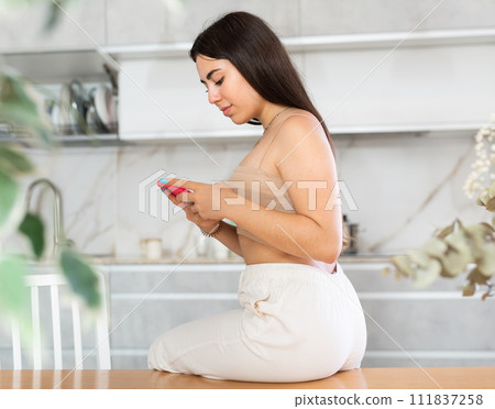 Young woman reading message on phone in kitchen 111837258