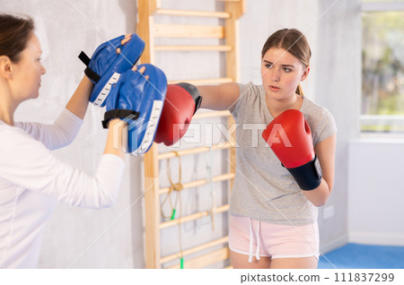Girls works out strength and speed of boxing punch mitts with help of partner in boxing paws Girls works out strength and speed of boxing punch mitts with help of partner in boxing paws 111837299