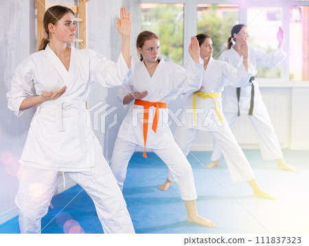 Team of teenage girls in kimonos uses new fighting techniques during karate lessons in gym 111837323