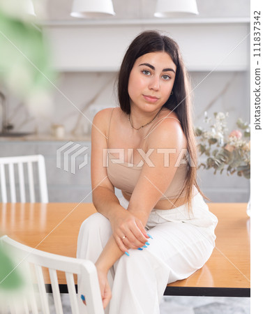 Smiling young woman posing sitting on kitchen table 111837342