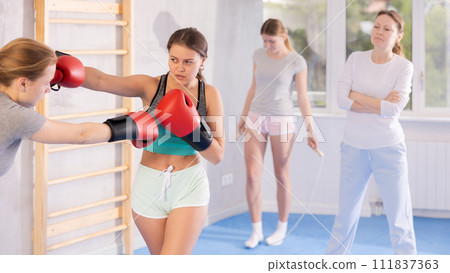 Adolescent girl in boxing gloves practicing punches in sparring during self defence course Adolescent girl in boxing gloves practicing punches in sparring during self defence course 111837363