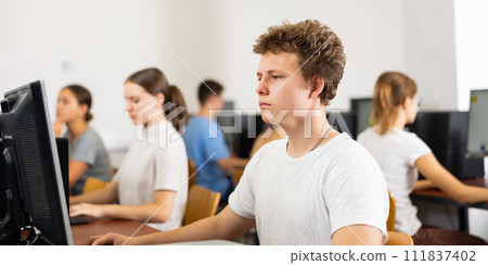 Focused teenager male student sitting at desk in computer class, preparing for exam 111837402