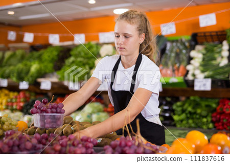 Fifteen-year-old girl who works part-time as a trainee saleswoman puts grapes on the counter 111837616