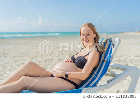 Basking in seaside tranquility, a pregnant woman lounges on a sun lounger, embracing the soothing ambiance of the beach for a moment of serene relaxation Basking in seaside tranquility, a pregnant woman lounges on a sun lounger, embracing the soothing ambiance of the beach for a moment of serene relaxation 111838893