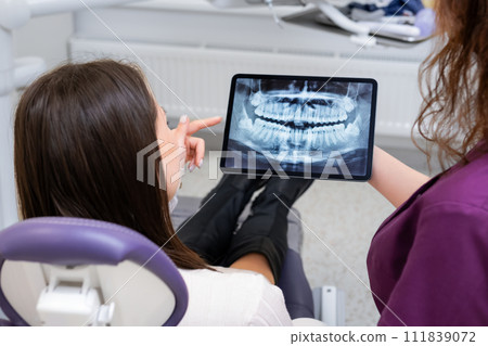 Dentist converses with the patient about treatment strategies while using a tablet to display the X ray image.  111839072