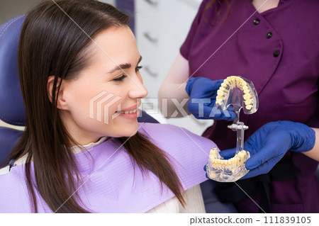 Dentist explains the procedure of alignment of teeth to the patient using a jaw layout in modern dentistry clinic 111839105