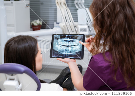 Showing the patient the X-ray, the female dentist explains the treatment concept during the discussion 111839106