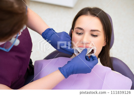 Orthodontist inserts a retractor into the mouth of the patient.  111839126