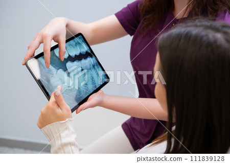 Dentist discussing tooth extraction procedure with patient showing x-rays.  111839128