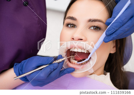 Woman patient undergoes dental treatment in clinic. Female dentist in gloves meticulously checks strength of teeth using specialized instruments Woman patient undergoes dental treatment in clinic. Female dentist in gloves meticulously checks strength of teeth using specialized instruments 111839166