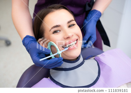 Dental assistant prepares patient for X-ray using specialized tools in clinic. Woman asks female patient to smile for better view of mouth Dental assistant prepares patient for X-ray using specialized tools in clinic. Woman asks female patient to smile for better view of mouth 111839181