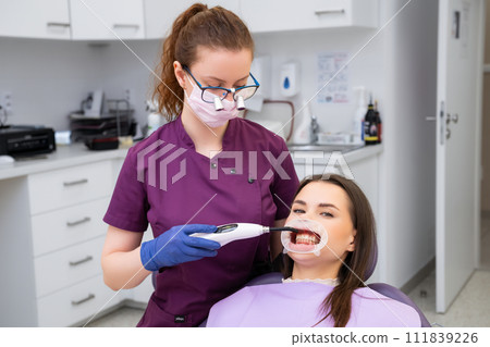 Dentist uses UV light completing dental filling procedure at appointment. UV light causes dental material to chemically bond with tooth enamel 111839226