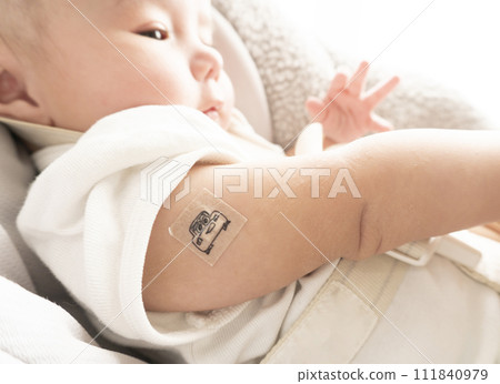 A 6-month-old baby boy with a bandage on his right arm for the injection site A 6-month-old baby boy with a bandage on his right arm for the injection site 111840979