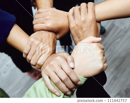 A close-up of a diverse team's hands interlocked, symbolizing unity, teamwork, and partnership 111842757