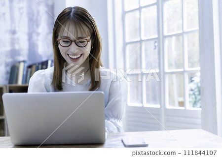 A young woman using a laptop in a bright room with sunlight shining through it A young woman using a laptop in a bright room with sunlight shining through it 111844107