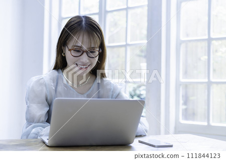 A young woman using a laptop in a bright room with sunlight shining through it A young woman using a laptop in a bright room with sunlight shining through it 111844123