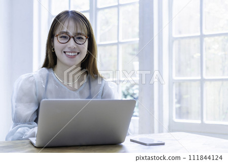 A young woman using a laptop in a bright room with sunlight shining through it A young woman using a laptop in a bright room with sunlight shining through it 111844124