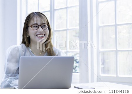 A young woman using a laptop in a bright room with sunlight shining through it A young woman using a laptop in a bright room with sunlight shining through it 111844126