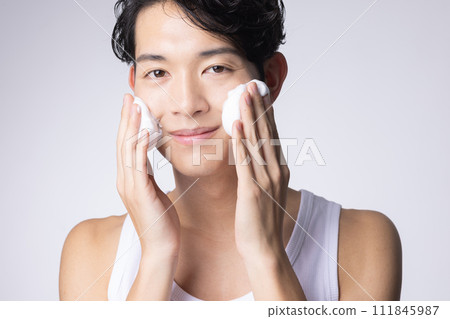 Portrait of a man washing his face and doing skin care on a white background 111845987