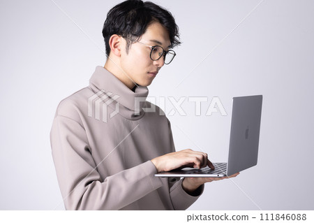 Image of a young man wearing glasses operating a PC Image of a young man wearing glasses operating a PC 111846088