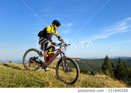 Cyclist man riding electric mountain bike outdoors. Male tourist biking along grassy trail in the mountains, wearing helmet and backpack. Concept of sport, active leisure and nature. 111846380