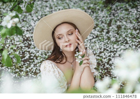 An attractive long-haired woman walks in the spring in the park of blooming apple trees. An attractive long-haired woman walks in the spring in the park of blooming apple trees. 111846478