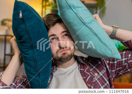 Irritated Caucasian tired bored man annoyed by noisy neighbors suffers from headache on couch Irritated Caucasian tired bored man annoyed by noisy neighbors suffers from headache on couch 111847016