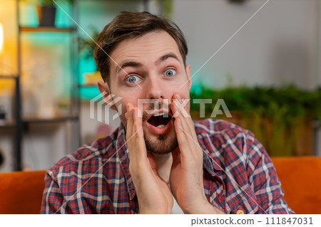 Amazed shocked man wow reaction open mouth looking at camera victory good win news at home room 111847031