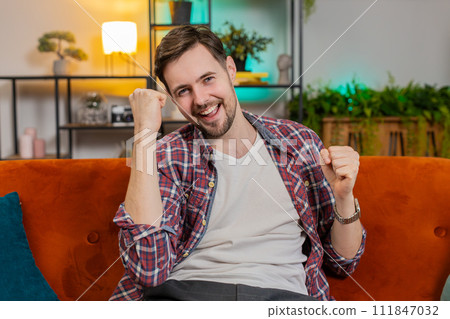 Happy Caucasian man watching TV shouting celebrating success winning goal achievement good news 111847032