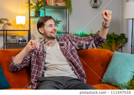 Man singing and dancing celebrate victory win enjoying music sitting on couch in living home room 111847038