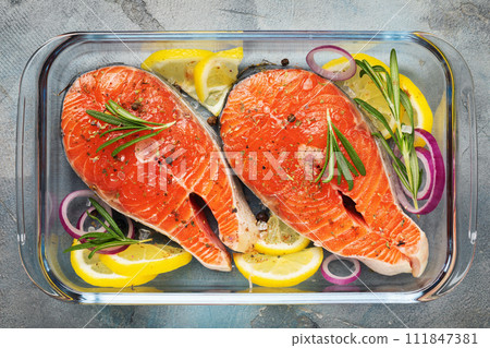Red fish steaks with various ingredients in a glass baking dish on the table, top view of fresh trout Red fish steaks with various ingredients in a glass baking dish on the table, top view of fresh trout 111847381