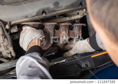 An auto mechanic installs an exhaust manifold to collect and remove exhaust gases from the cylinders of a passenger car engine after replacing the gasket 111847388