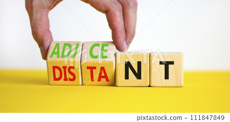 Adjacent or distant symbol. Businessman turns beautiful wooden cubes and changes word Distant to Adjacent. Beautiful yellow table white background. Copy space. Business adjacent or distant concept. 111847849