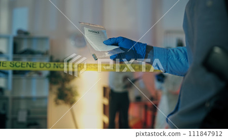A detective in protective gloves is holding a bullet in an evidence bag, examining its caliber A detective in protective gloves is holding a bullet in an evidence bag, examining its caliber 111847912