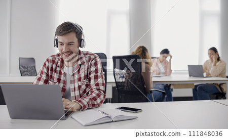 Excited young man in headphones working on laptop in office, online music app 111848036