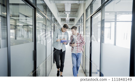 Male designers discussing work, walking in office corridor, advertising agency 111848149