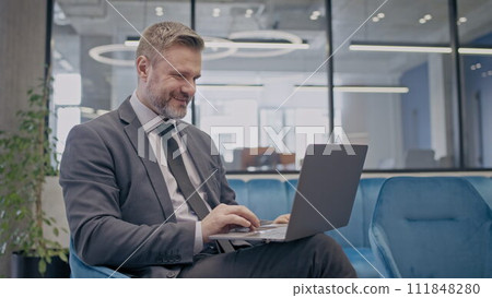 Successful businessman working on laptop, sitting in comfortable office and smiling Successful businessman working on laptop, sitting in comfortable office and smiling 111848280