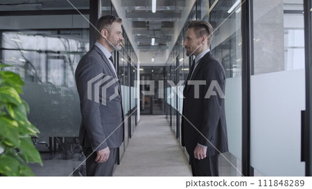 Smiling company boss giving instruction to employee in office corridor, teamwork Smiling company boss giving instruction to employee in office corridor, teamwork 111848289