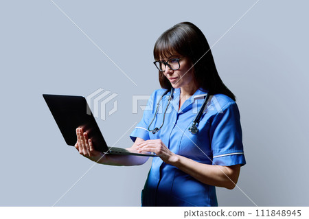 Female nurse using laptop, profile view on gray studio background 111848945