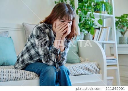 Upset sad young female sitting on couch at home Upset sad young female sitting on couch at home 111849001