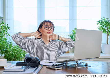 Tired middle-aged woman sitting at her workplace, desk with computer Tired middle-aged woman sitting at her workplace, desk with computer 111849041