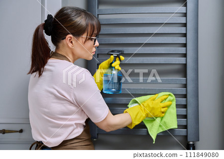 Woman doing house cleaning in bathroom, cleaning dust from heated towel rail Woman doing house cleaning in bathroom, cleaning dust from heated towel rail 111849080