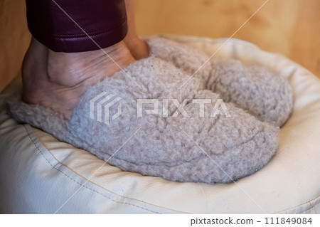 A person feet in soft woolen slippers, resting on a cushioned seat. 111849084