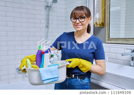Middle-aged woman in gloves with basin of detergents in bathroom Middle-aged woman in gloves with basin of detergents in bathroom 111849109
