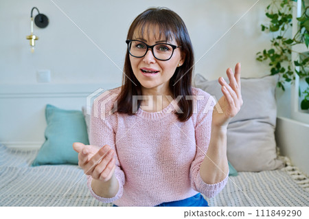Webcam view of middle-aged woman talking, sitting on couch at home Webcam view of middle-aged woman talking, sitting on couch at home 111849290