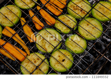 Chopped zucchini and carrots roasting on fire seasoned with aroma herbs and spices. Delicious fresh vegetables grilling on barbecue smoker grid. Diet vegan bbq. Outdoor recreation Chopped zucchini and carrots roasting on fire seasoned with aroma herbs and spices. Delicious fresh vegetables grilling on barbecue smoker grid. Diet vegan bbq. Outdoor recreation 111849332